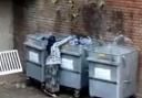 A still image from the video showing a woman rifling through bins in Lye
